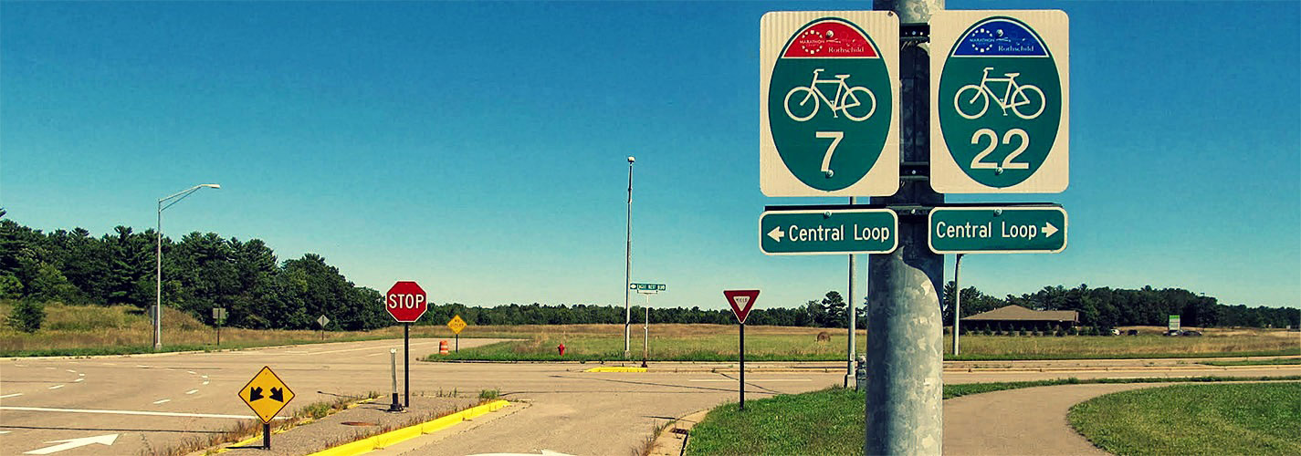 Two bicycle signs showing Central Loop near a stop sign on a rural road